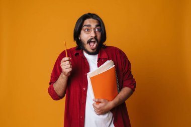 Sarı arka planda izole edilmiş ders kitaplarını tutan heyecanlı Hintli genç adam.