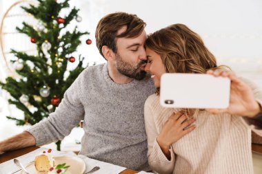 Romantik, neşeli bir çift cep telefonuyla öpüşüyor ve selfie çekiyor.