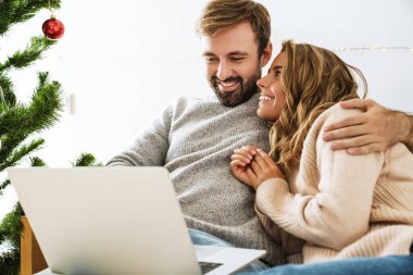 Güzel mutlu çift rahat bir odada dinlenirken dizüstü bilgisayar kullanıyor.