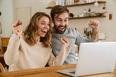 Güzel heyecanlı çift, rahat bir mutfakta dizüstü bilgisayar kullanırken güzel bir jest yapıyor.