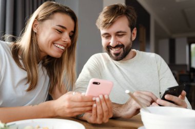 Mutlu genç çift kahvaltıda cep telefonu kullanıyor.