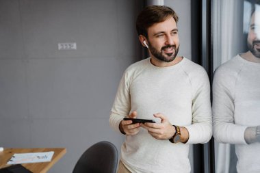 Kapalı mekanda cep telefonu kullanan kulaklıklı yakışıklı adam.