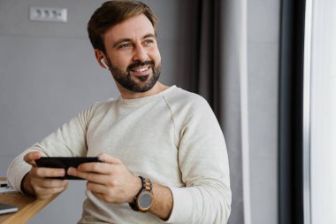 Evde otururken cep telefonu kullanan kulaklıklı yakışıklı adam.