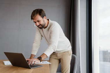 Ev içinde dizüstü bilgisayarla çalışan kulaklıklı yakışıklı adam.