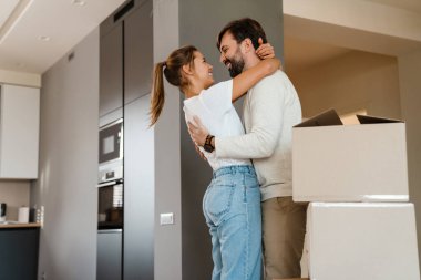 Yeni dairede karton kutuların yanında durup gülümseyen ve sarılan güzel bir çift.