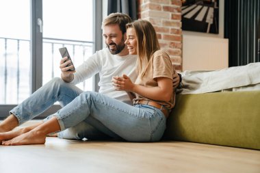 Mutlu güzel çift evde dinlenirken cep telefonu kullanıyor.