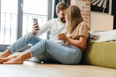 Mutlu güzel çift evde dinlenirken cep telefonu kullanıyor.