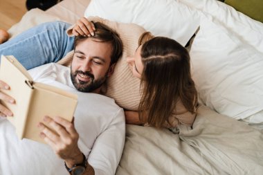 Mutlu genç çift evde yatarken kitap okuyor.