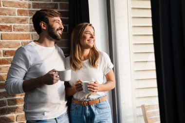 Mutlu genç ve çekici bir çift evlerinin penceresinde dikilirken kahve içiyorlar.