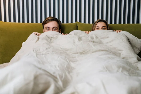 Glückliches Junges Paar Guckt Aus Der Decke Während Bett Liegt — Stockfoto