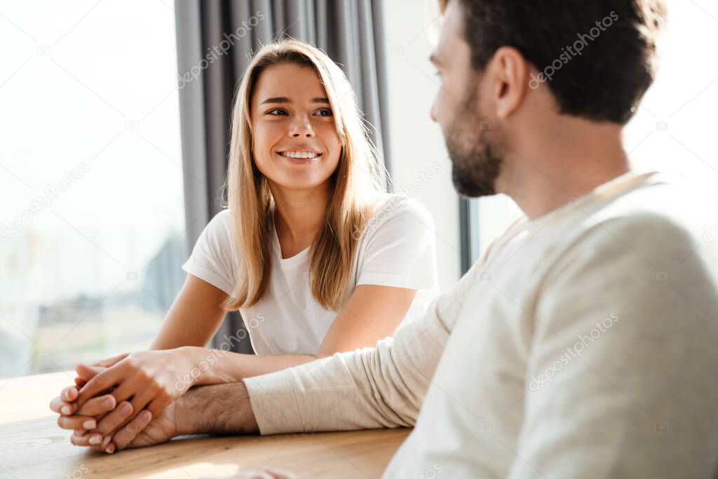 Young couple in love sharing a tender moment clasping hands while sitting at the table and smiling into each others eyes