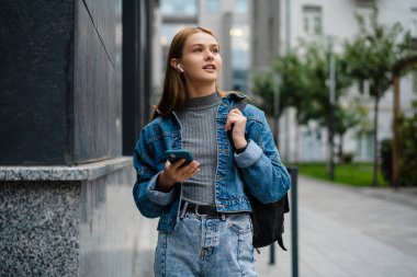 Şehir caddesinde yürürken cep telefonu kullanan kulaklıklı hoş bir öğrenci kız.