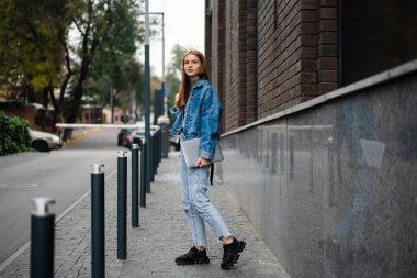 Güzel sarışın kız gülümseyen ve elinde dizüstü bilgisayarla caddede dikilirken