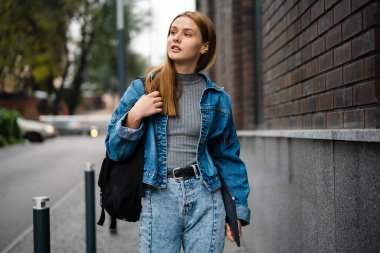 Kot pantolon giyen güzel genç bir kadın sokakta yürüyor, dizüstü bilgisayar taşıyor.