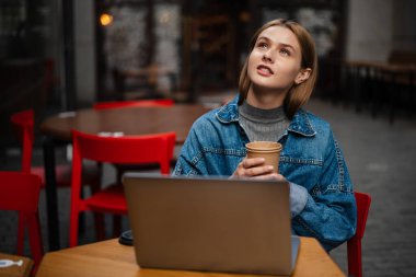 Sokak kafesinde dizüstü bilgisayarla çalışırken kahve içen güzel odaklı öğrenci kız.