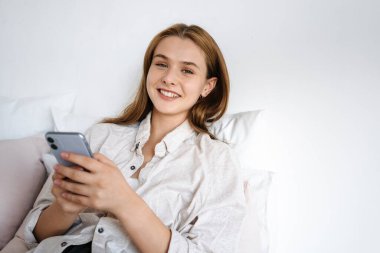 Güzel gülümseyen güzel kız evde dinlenirken cep telefonu kullanıyor.