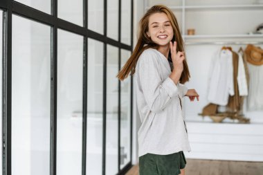 Güzel, neşeli, güzel bir kız. Gülümsüyor ve evdeki gardıropta barış işareti yapıyor.