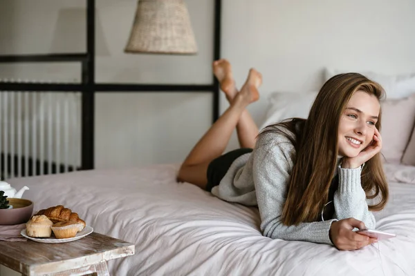 Güzel gülümseyen güzel kız evde yatarken cep telefonu kullanıyor.