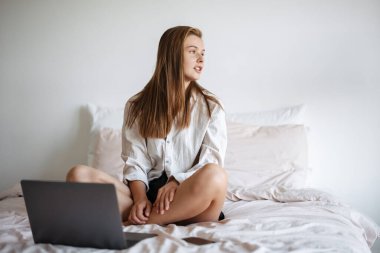 Güzel memnun güzel kız evde cep telefonu ve dizüstü bilgisayar kullanıyor.