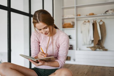 Güzel, neşeli, güzel kız evde gardırop başında otururken notlar yazıyor.