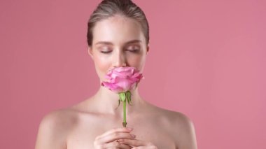 Çekici genç bir kadın stüdyoda pembe arka planda duran gül çiçeğinin kokusunu alıyor.
