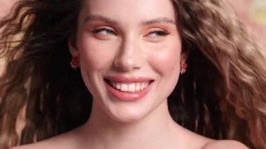 Saçları rüzgarda dalgalanırken ve stüdyoda çiçeklerle kaplı bir arka planda dikilirken muhteşem genç bir kadının yakın çekim görüntüsü kameraya poz veriyor.