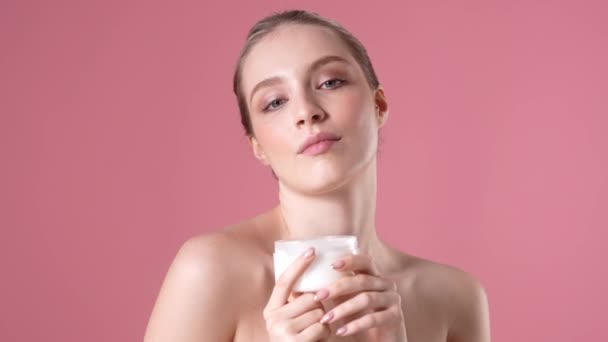 一位快乐的年轻女子站在工作室的粉红背景上 一边在自己的身体上涂上药膏 一边摆姿势 — 图库视频影像