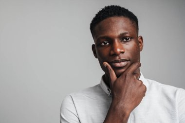 Gri arka planda izole edilmiş bir şey hakkında derin düşünen Afrikalı genç bir adamın yakın plan portresi.