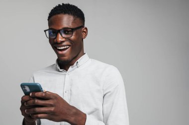 Yakışıklı, gülümseyen Afrikalı iş adamı. Gri arka planda izole edilmiş, beyaz resmi tişört giyen cep telefonu kullanıyor.