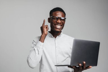 Yakışıklı, gülümseyen bir Afrikalı iş adamı. Gri arka plan üzerinde izole edilmiş dizüstü bilgisayar kullanıyor. Beyaz resmi gömlek giyiyor.