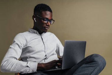 Gri arka planda izole bir şekilde otururken dizüstü bilgisayarda çalışan kendine güvenen yakışıklı iş adamı.