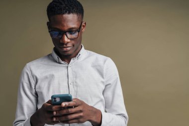 Gri arka planda izole edilmiş, beyaz resmi tişörtlü, cep telefonu kullanan yakışıklı, kendine güvenen Afrikalı işçiler.