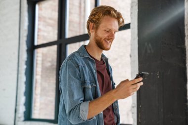 Mutlu yakışıklı kızıl adam gülümsüyor ve cep telefonunu içeride kullanıyor.