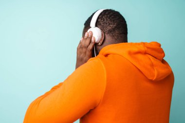 Mavi arka planda izole edilmiş kulaklıklı müzik dinleyen Afrikalı Amerikalı bir adam.