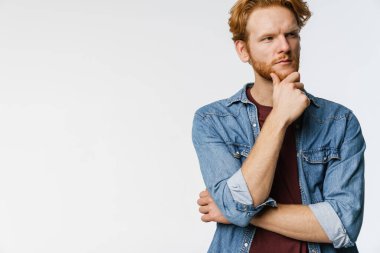 Düşünceli, yakışıklı, beyaz arka planda poz veren ve bir kenara bakan kızıl adam.