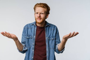 Kafası karışık, kızıl saçlı adam beyaz arka planda yalnız poz veriyor ve kameraya bakıyor.