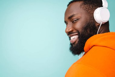Neşeli Afrikalı Amerikalı adam mavi arka plandan izole edilmiş kulaklıklarla müzik dinliyor.