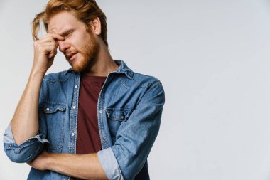 Başı ağrıyan, kameraya poz veren mutsuz kızıl adam beyaz arka planda izole edilmiş.