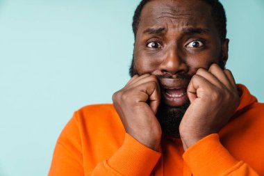 Korkmuş Afrikalı Amerikalı adam mavi arka planda yalnız poz veriyor ve kameraya bakıyor.