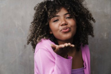Neşeli, hoş, Afro-Amerikalı bir kadın. Gri duvarın üzerinden hava öpücüğü üflüyor.