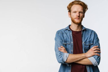 Ciddi yakışıklı kızıl adam poz veriyor ve kolları çapraz beyaz arka planda.