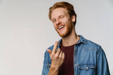 Neşeli kızıl saçlı adam ararken gülümsüyor ve beyaz arka planda izole bir şekilde işaret ediyor.