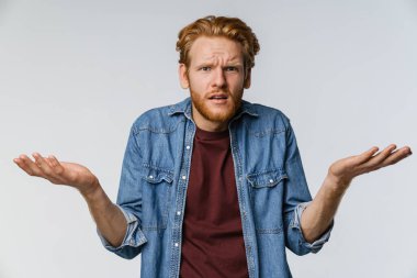 Kafası karışık, kızıl saçlı adam beyaz arka planda yalnız poz veriyor ve kameraya bakıyor.