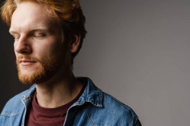 Yakışıklı, tıraşsız, kızıl saçlı, gözleri kapalı poz veren, gri arka planda izole edilmiş.