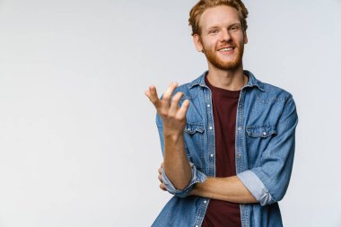 Mutlu yakışıklı adam gülümsüyor ve beyaz arka planda izole edilmiş kamerayı işaret ediyor.