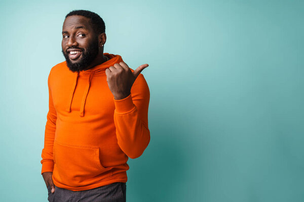 Happy african american man smiling and pointing finger aside isolated over blue background