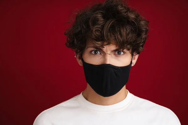 Caucasian angry guy in face mask posing and looking at camera isolated over red background