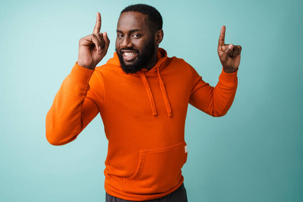 Happy african american man smiling and pointing fingers upward isolated over blue background