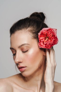 Gri arka planda izole edilmiş, elinde çiçekle poz veren güzel yarı çıplak kadın.