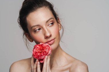 Gri arka planda izole edilmiş, elinde çiçekle poz veren güzel yarı çıplak kadın.